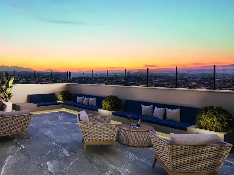 Lounge externo do rooftop do Jóquei Condomínio Clube ao pôr do sol, com sofás, poltronas e vista da cidade