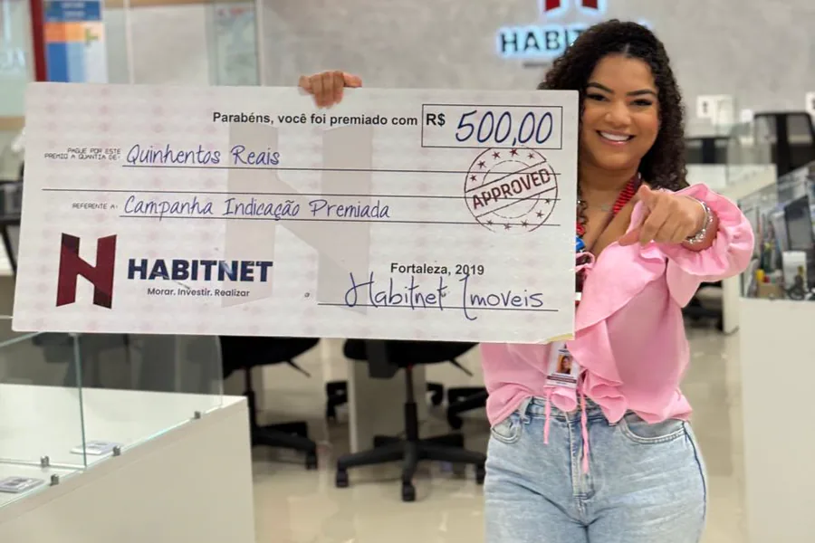 Cliente da Habitnet segurando o cheque simbólico de R$ 500 da campanha Indicação Premiada